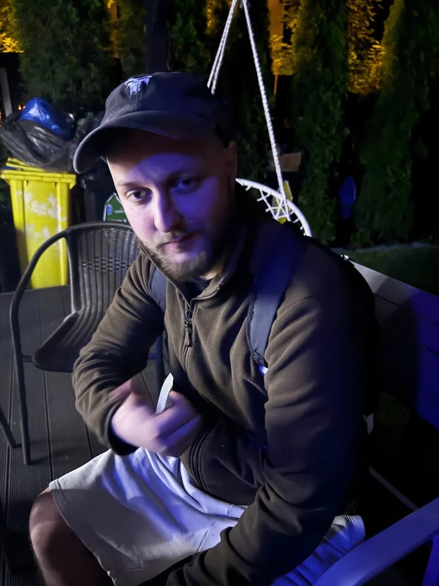Luca sitting outdoors at night wearing a black cap and backpack.
